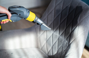 Dry cleaning gray soft chairs made of fabric upholstery with a washing vacuum cleaner. Cleaning company services, close-up