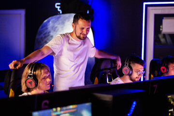 Happy E-sport coach laughs during game of his team in cyber sport tournament. Different ages gamers...