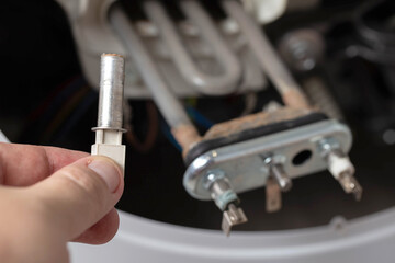 The master holds in his hand an electric temperature sensor for heating water in the washing machine, close-up