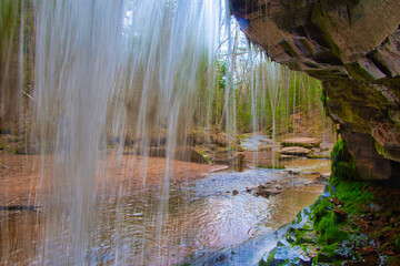 Landscape of a small waterfall viewed from behind as it cascades into Lost Creek in a peaceful forest on an early Spring day near Cornucopia, Wisconsin.