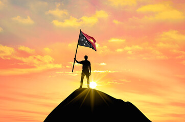 Waving flag of Papua New Guinea at the top of a mountain summit against sunset or sunrise. Papua New Guinea flag for Independence Day.