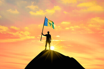 Waving flag of Saint Vincent at the top of a mountain summit against sunset or sunrise. Saint...