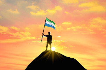 Waving flag of Sierra Leone at the top of a mountain summit against sunset or sunrise. Sierra Leone flag for Independence Day.