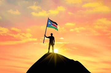 Waving flag of South Sudan at the top of a mountain summit against sunset or sunrise. South Sudan flag for Independence Day.