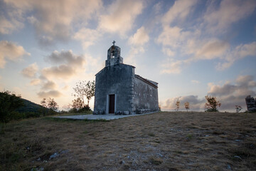 Small historic church with a path leading to it. The church stands on a cliff in the sunrise and in a Mediterranean landscape. Historic mountain village of Bresc, Istria, Croatia