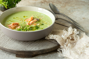 bowl with creamy soup of zucchini, broccoli and salmon on the table
