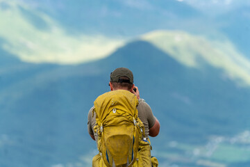 male backpacking hiker with yellow backpack climbing Romsdalseggen trail in Andalsnes Norway in summer with rocky mountains in the background