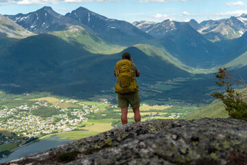 male backpacking hiker with yellow backpack climbing Romsdalseggen trail in Andalsnes Norway in summer with rocky mountains in the background