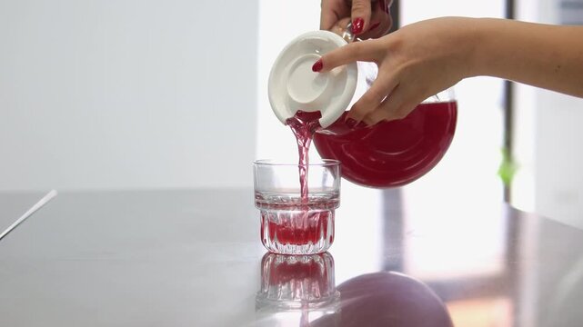 Woman pouring healthy cranberry juice from bottle into glass on color Carafe of fruit compote. A woman's hand pours compote into a glass.