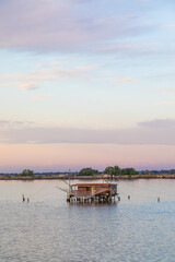 Italy, Comacchio lagoon. Panorama with traditional house for fishing at sunset, blue sky