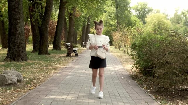 A teenage girl walks confidently through a sunny park on a spring day in stylish school clothes and glasses. Teenage fashion and style concept.