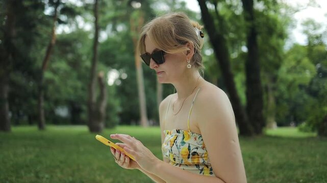 Gorgeous blonde Caucasian lady using smart phone having picnic and making selfie outdoors at warm sunny day in the park. Beautiful young woman enjoying life outdoors. High quality FullHD footage