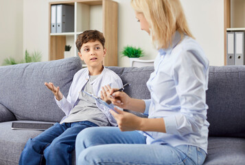Female child psychologist talking to boy sitting on couch at home. Social and mental therapy support for children and teenagers at school.