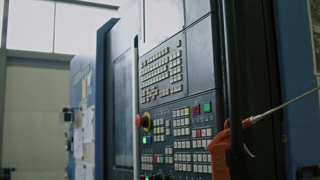 No people side tilt shot of large industrial control panel with buttons and screen, air blow gun hanging on handle in production plant