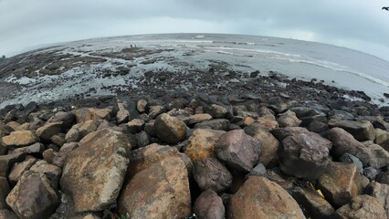 A picturesque landscape featuring a rocky beach shore, the sea gently lapping at the rocks beneath a bright sky.