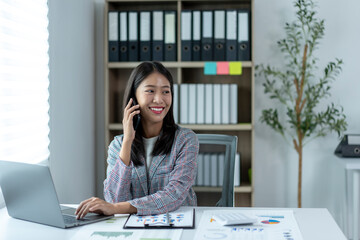 A woman is sitting at a desk with a laptop and talking on a cell phone