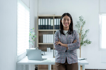 A woman is standing in front of a desk with a laptop and a stack of papers
