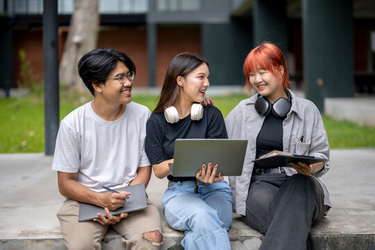 Three young people are sitting on a cement ledge, one of them holding a laptop