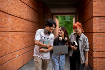 Three young people are walking down a brick hallway, each carrying a laptop