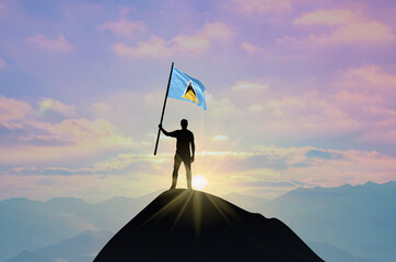 Waving flag of Saint Lucia at the top of a mountain summit against sunset or sunrise. Saint Lucia flag for Independence Day.