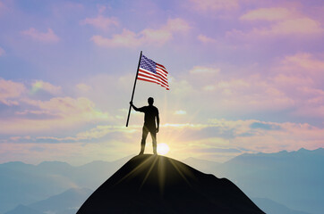 Waving flag of America at the top of a mountain summit against sunset or sunrise. American flag for...