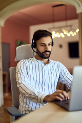A male wearing headphones, typing on a laptop, working as a freelancer in the co-working space.