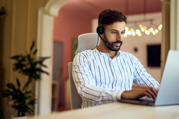 A focused freelancer, working over the laptop, sending some e-mails, and wearing headphones.