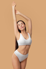 Obraz premium Beautiful woman with perfect skin in underwear posing on beige background. Body care