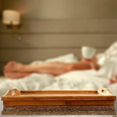 Close up of wooden table with empty tray with copy space for products. Blurred woman drinking coffee in bed background.  Breakfast in bed concept. 3 d rendering.  