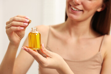 Fototapeta premium Aromatherapy. Woman with bottle of essential oil on light background, closeup