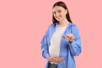 Expecting twins. Pregnant woman holding two pacifiers on pink background, space for text