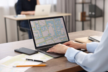 Cartographer working with cadastral map on laptop at wooden table in office, closeup