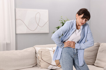 Upset woman suffering from abdominal pain at home, space for text