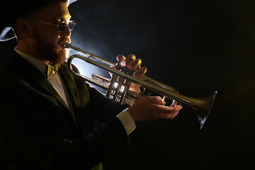 Obraz premium Professional musician playing trumpet on black background in smoke