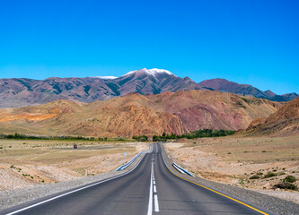 Empty asphalt road in front of huge majestic mountains with snow covered peaks. Beautiful landscape of Altay region, Russia.