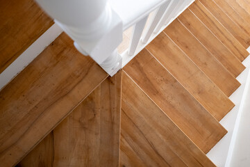 Top-down view of a wooden staircase with white railings, showcasing the clean lines and contrast of materials, creating a visually appealing and modern interior feature.