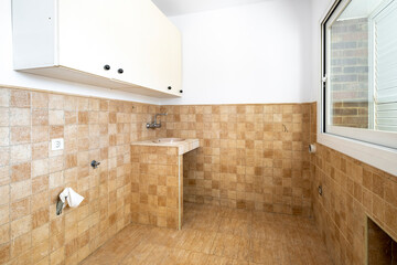 A vacant kitchen showcasing tiled walls in a warm beige color, a simple sink with under-sink plumbing, and a large window providing natural light.