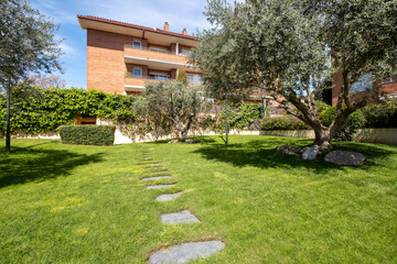 The image shows a lush green garden with carefully placed stepping stones leading through vibrant grass, complemented by well-maintained trees in the background.