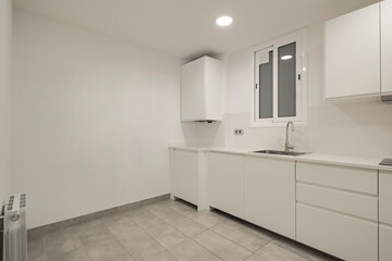 A contemporary white kitchen with modern fixtures and a window providing natural light, showcasing a minimalist design perfect for a sleek and functional cooking space.
