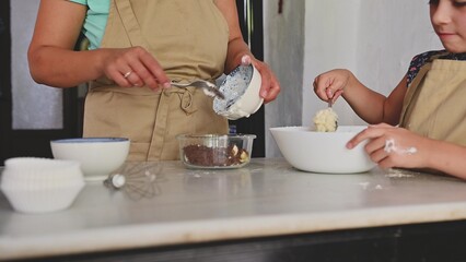 Mother and child baking together in the kitchen with aprons and bowls of ingredients