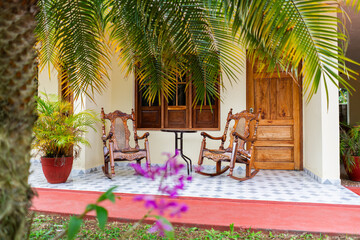 Obraz premium Two rocking chairs in front of a tropical house in the Latin American Caribbean with palms trees 