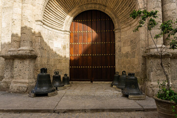 old stone church entrance with majestic wooden door and antique steel bells in Havana Cuba