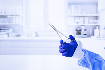 A person is holding a pair of scissors in a blue glove. The image has a sterile, clinical feel to it, with a white background and shelves full of medical supplies
