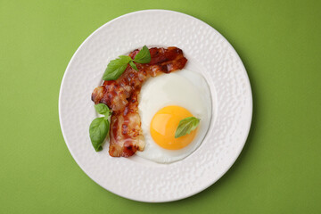 Fried egg, bacon and basil on green background, top view