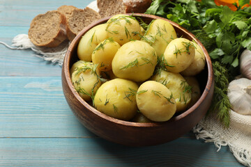 Tasty young boiled potatoes with dill in bowl on light blue wooden table