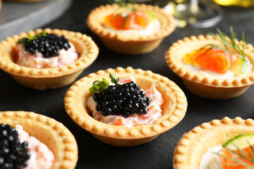 Delicious canapes with salmon and caviar on black table, closeup