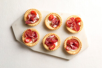 Delicious canapes with jamon, cream cheese and cherry tomatoes on white table, top view