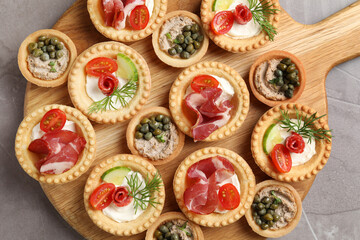 Delicious canapes with jamon, pate and dry smoked sausages on grey textured table, top view