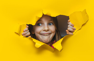 A funny laughing red-haired girl looks out through a hole in yellow paper. The concept of surprise,...