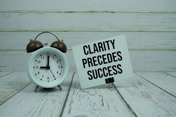 Clarity Precedes Success text on paper card with alarm clock on wooden background